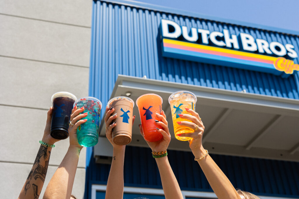 Hands raise five colorful Dutch Bros drinks outside a Dutch Bros Coffee location during an Eddy House Giveback Day fundraiser in Reno, Nevada.
