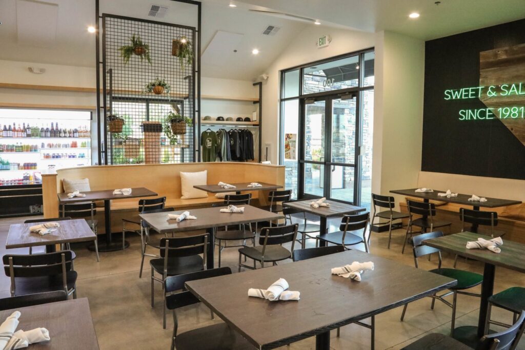 Interior of The Cheese Board’s Wedge Parkway location in Reno, featuring wooden tables, black chairs, booth seating, and hanging plants.